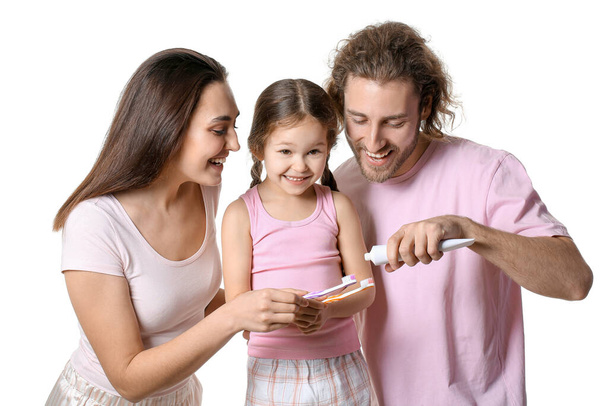 Jeune homme appliquant de la pâte dentaire sur les brosses de sa femme et sa fille sur fond blanc - Photo, image
