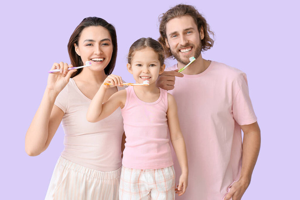 Маленька дівчинка з батьками чистить зуби на бузковому фоні
 - Фото, зображення