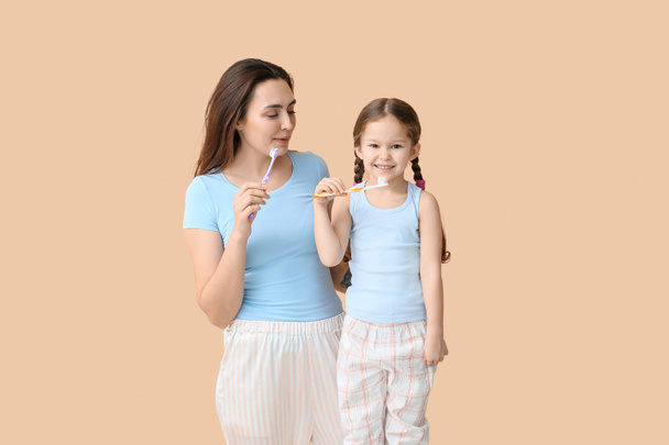 Little girl with her mother brushing teeth on beige background - Фото, зображення