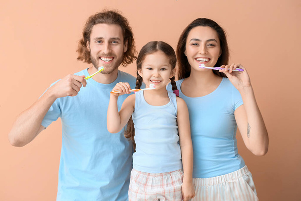 Mała dziewczynka z rodzicami myjąca zęby na beżowym tle - Zdjęcie, obraz