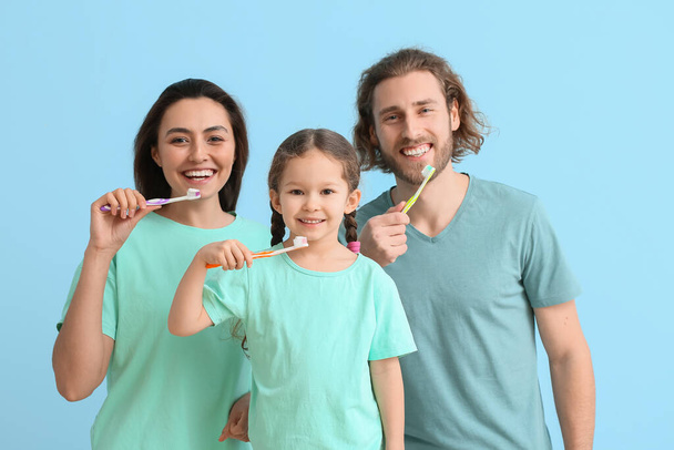 Kleines Mädchen mit ihren Eltern beim Zähneputzen auf blauem Hintergrund - Foto, Bild
