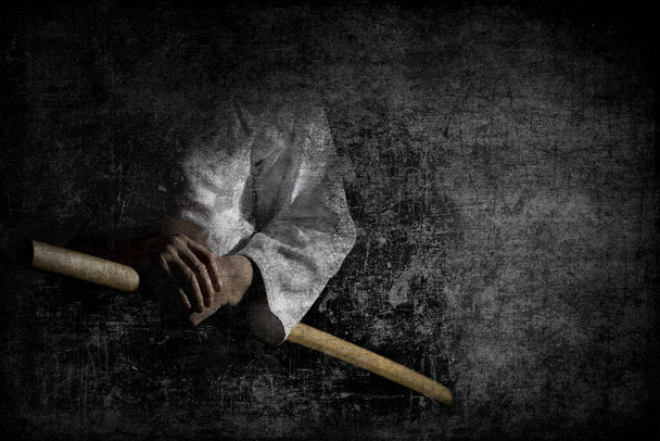 Человек в черном Хакама стоит в боевой позе с деревянным мечом боккен на темном фоне гранж. - Фото, изображение