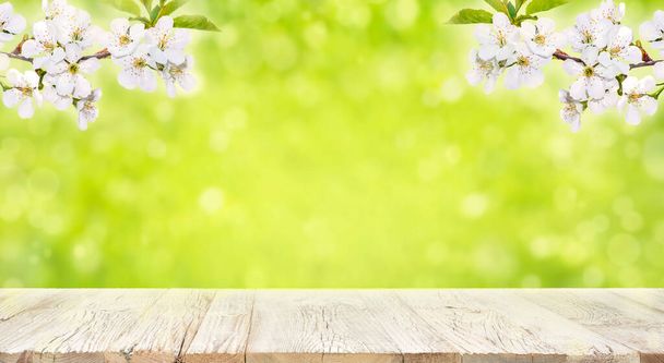 Old vintage planked wood table in perspective on bright green bokeh spring background with blooming branch. - Photo, Image