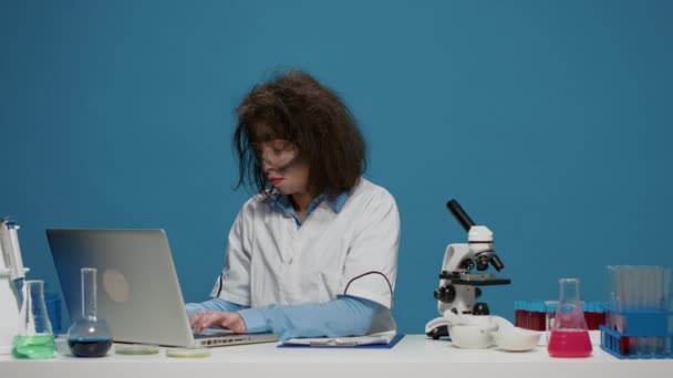Goofy científico loco utilizando el ordenador portátil y documentos en la cámara - Imágenes, Vídeo