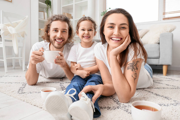 Young family with cups of tea resting on carpet at home - Photo, Image