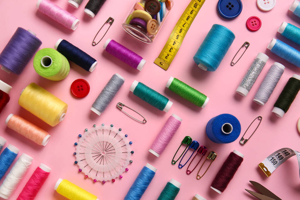 Draadspoelen, kogelpennen, meetlint en toetsen op roze achtergrond - Foto, afbeelding
