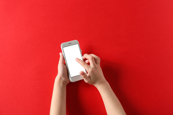 Niño usando el teléfono móvil moderno sobre fondo rojo - Foto, Imagen