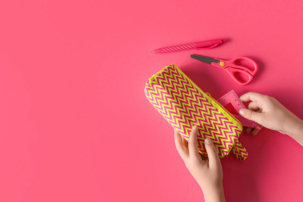 Manos de niño con estuche de lápiz y papelería sobre fondo rosa - Foto, imagen