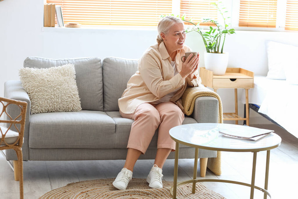 Mujer madura bebiendo té caliente mientras está sentada en el sofá - Foto, imagen