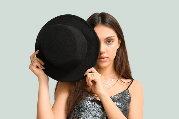 Giovane donna con trucco creativo volto di chiusura con elegante cappello su sfondo chiaro - Foto, immagini