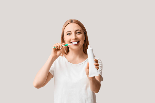 Piękna dojrzała kobieta myje zęby na jasnym tle - Zdjęcie, obraz