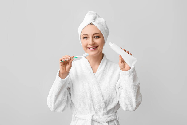 Belle femme mature en peignoir, avec brosse à dents et pâte sur fond clair - Photo, image