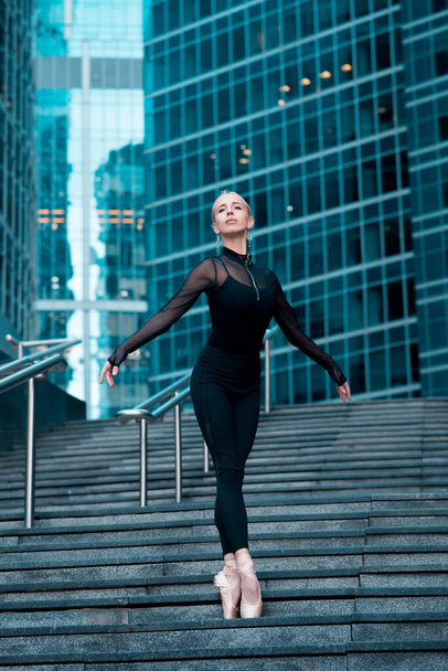 Изящный артист балета, балерина, стоящая на ступеньках, лестница. Городской фон - Фото, изображение