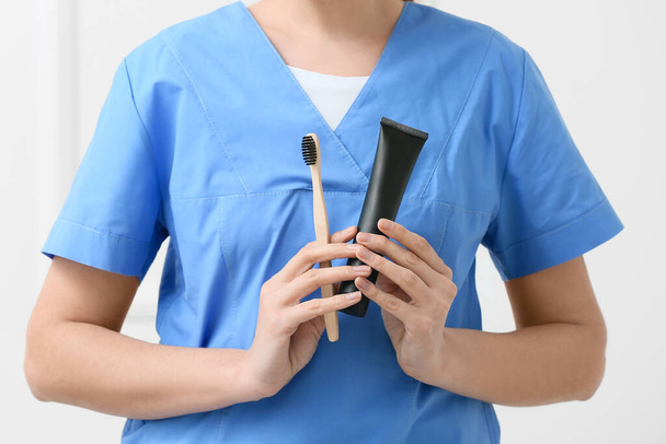Female dentist with activated charcoal tooth paste and brush on light background, closeup - Photo, image