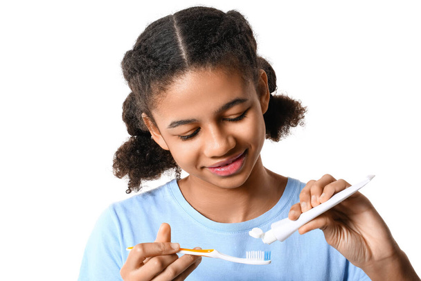 African-American teenage girl applying tooth paste onto brush on white background - Photo, Image