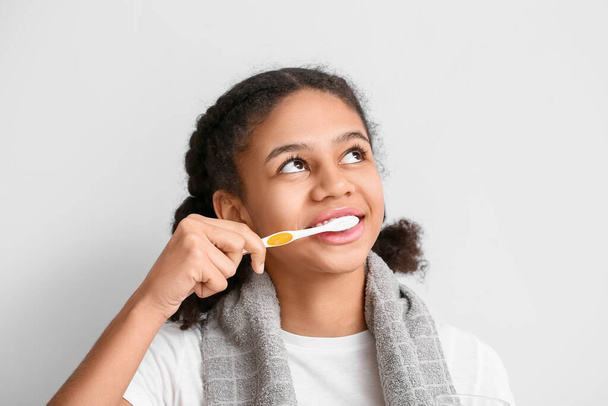 Afro-amerikanisches Teenager-Mädchen beim Zähneputzen auf hellem Hintergrund - Foto, Bild