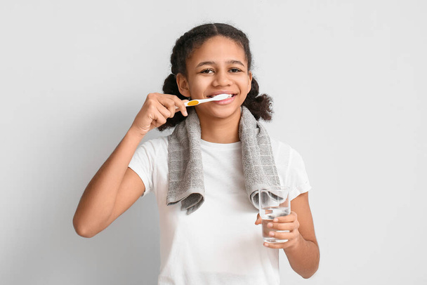Afro-americano ragazza adolescente con vetro di acqua lavarsi i denti su sfondo chiaro - Foto, immagini