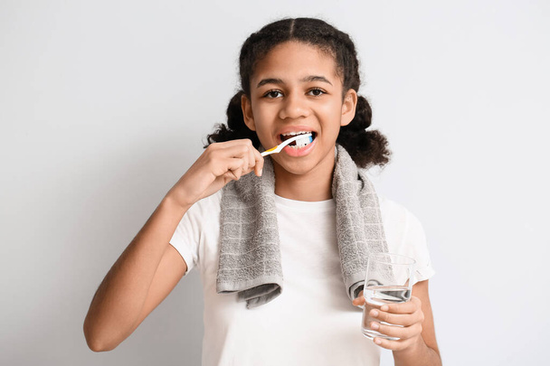 Afroamerykańska nastolatka ze szklanką wody myjącej zęby na jasnym tle - Zdjęcie, obraz