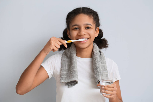 Africko-americké dospívající dívka se sklenicí vody kartáčování zubů na světlém pozadí - Fotografie, Obrázek