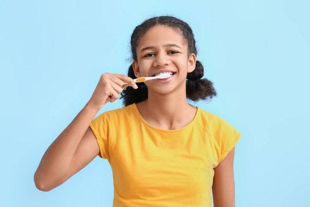 Mavi arka planda dişlerini fırçalayan Afro-Amerikalı genç kız. - Fotoğraf, Görsel
