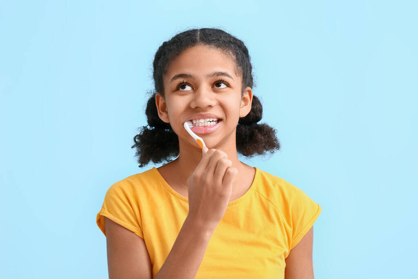 African-American teenage girl brushing teeth on blue background - Fotó, kép
