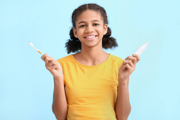 Mavi arka planda diş fırçası ve yapıştırıcısı olan Afro-Amerikalı bir genç kız. - Fotoğraf, Görsel