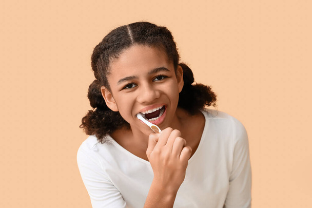 African-American teenage girl brushing teeth on beige background - Фото, зображення