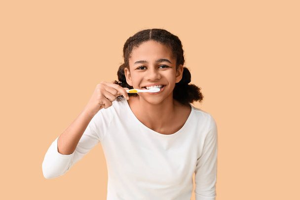 Adolescente afroamericana cepillándose los dientes sobre fondo beige - Foto, Imagen