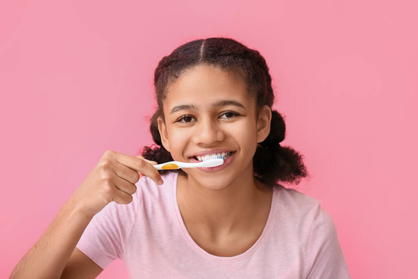 Afro-Amerikaanse tiener meisje poetsen tanden op roze achtergrond - Foto, afbeelding