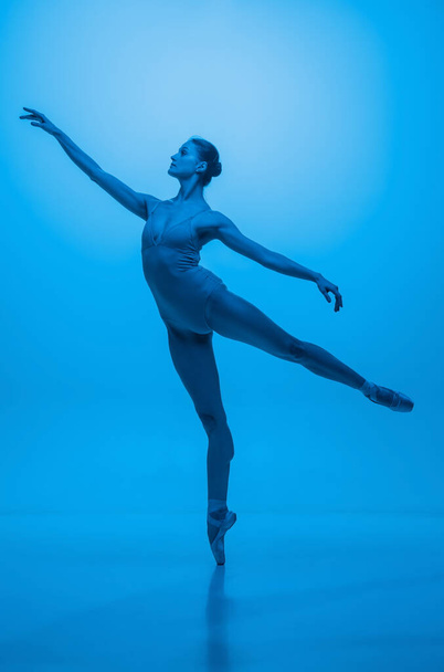 Young and graceful ballet dancer isolated on blue studio background in neon light. Art, motion, action, flexibility, inspiration concept. - Foto, Imagen