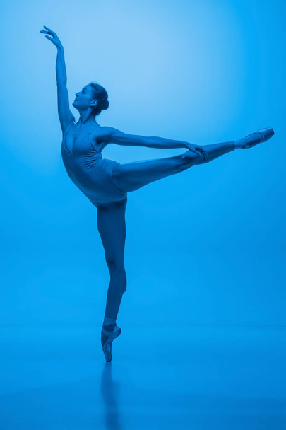 Junge und anmutige Balletttänzerin isoliert auf blauem Studiohintergrund in Neonlicht. Kunst, Bewegung, Aktion, Flexibilität, Inspirationskonzept. - Foto, Bild