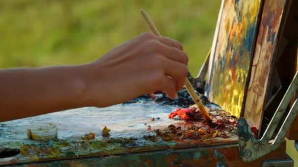 Onbekende kunstenaar mengt verf op het palet. Close-up handtekening op doek buiten - Video