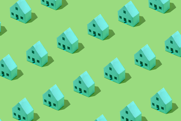Diagonale rijen van kleine groene modelhuizen gerangschikt als een herhaling patroon op een bijpassende groene achtergrond - Foto, afbeelding
