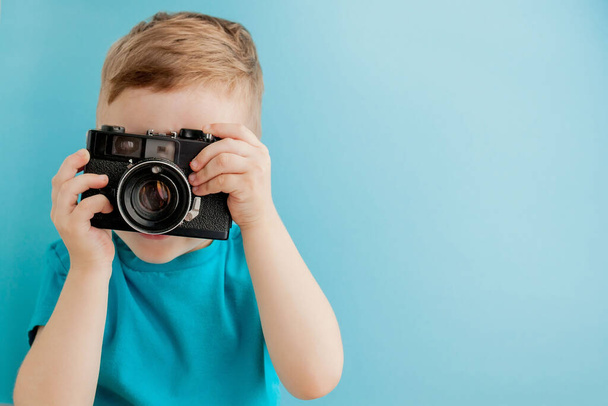 Little boy with an old camera on a blue background. - Φωτογραφία, εικόνα