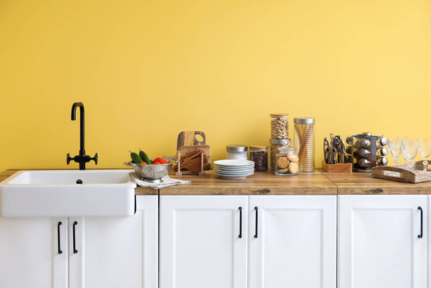 Mostradores con fregadero, comida y utensilios de cocina cerca de la pared amarilla - Foto, Imagen