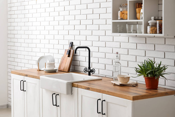 Contadores com pia, planta de sala e utensílios de cozinha perto da parede de tijolo branco - Foto, Imagem