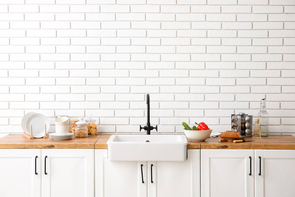 Счетчики с раковиной, пищевой и кухонной утварью возле стены из белого кирпича - Фото, изображение