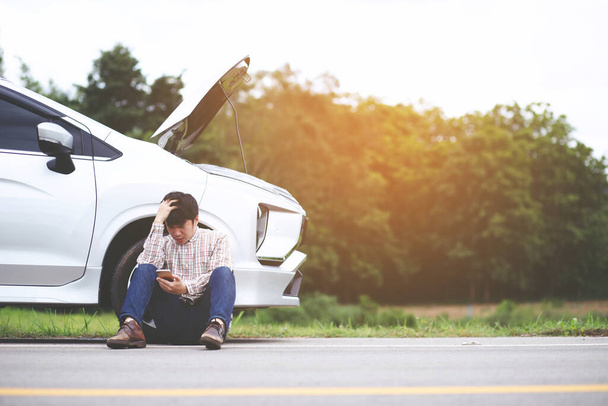 Злий чоловік стоїть перед зламаною машиною, яка закликає допомогти
 - Фото, зображення