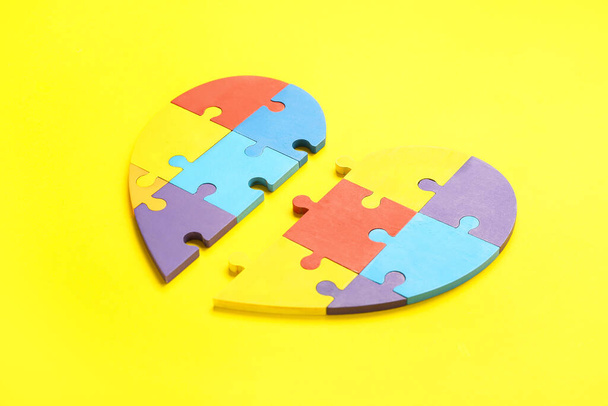 Corazón hecho de piezas de rompecabezas de colores sobre fondo amarillo. Concepto de trastorno autista - Foto, imagen