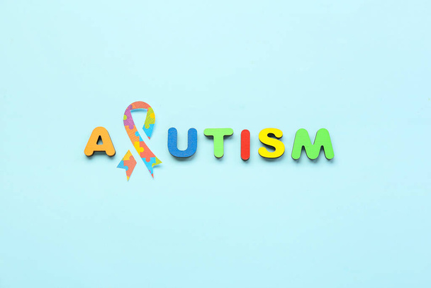 Word AUTISM with paper awareness ribbon on blue background - Photo, Image