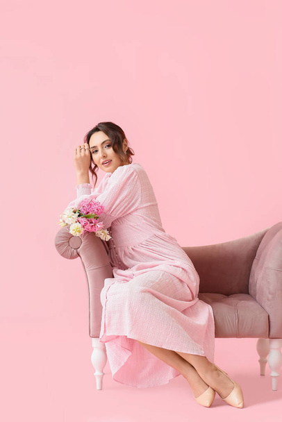 Bella giovane donna con fiori di giacinto seduta sul divano sullo sfondo rosa - Foto, immagini