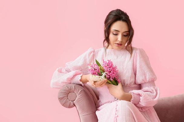 Pretty young woman with hyacinth flowers sitting on sofa against pink background - Foto, immagini