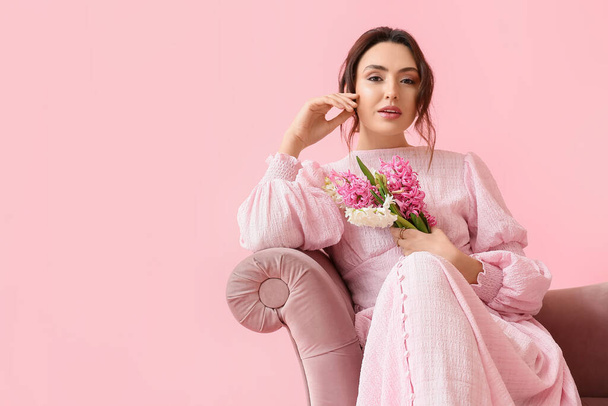 Bella giovane donna con fiori di giacinto seduta sul divano sullo sfondo rosa - Foto, immagini
