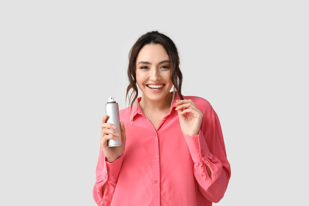 Mujer bastante joven con spray para el cabello sobre fondo gris - Foto, imagen
