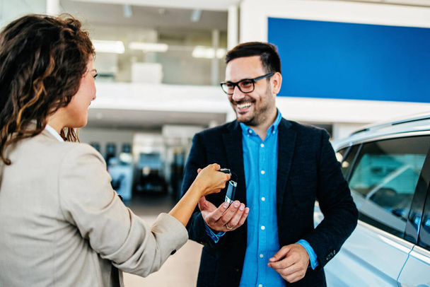 Happy middle age businessman buying new and expensive car. Beautiful female dealer helps him to make right decision. She gives him car keys. - Zdjęcie, obraz