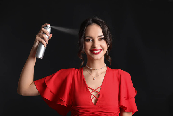 Beautiful young woman with hair spray on black background - Foto, imagen