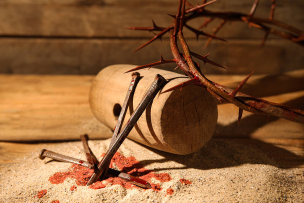 Korona cierniowa z gwoździami, młotkiem, kroplami krwi i piaskiem na drewnianym tle - Zdjęcie, obraz