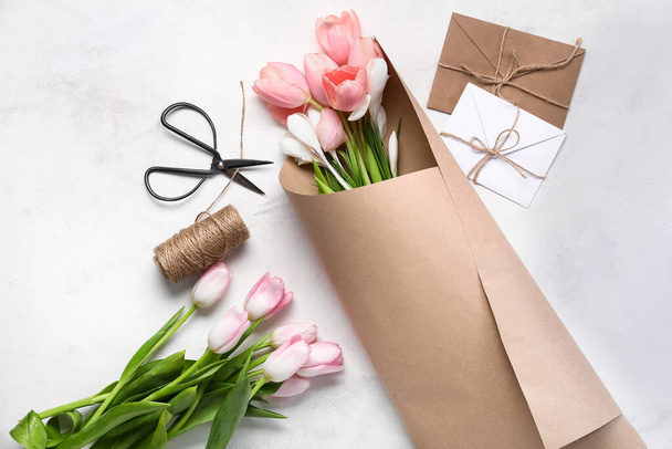 Prachtige lentebloemen in inpakpapier, schaar, touw en enveloppen op lichte ondergrond - Foto, afbeelding