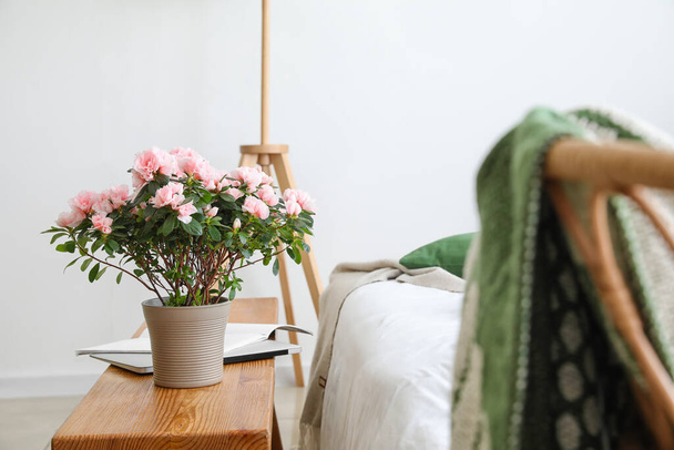 Квіти бегонії, ноутбук і журнал на столі біля ліжка в світлій кімнаті
 - Фото, зображення