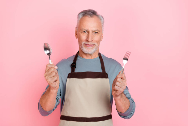 Photo of funny charming retired man wear grey shirt apron holding fork spoon isolated pink color background - Foto, Bild